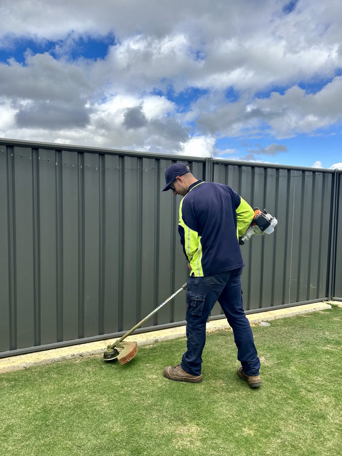 Mitch edging a back lawn with a line trimmer along a colorbond fence